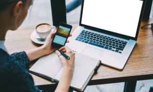 Person working at desk with laptop, smartphone, notebook and coffee