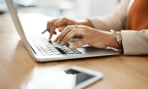 Woman typing on laptop with smartphone on desk